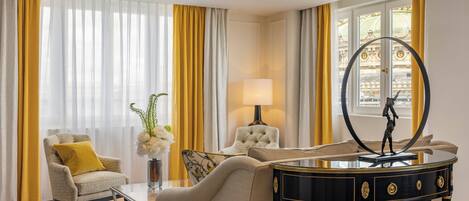 Un salón bien iluminado con un sofá, un sillón y una mesa de centro. Hay una lámpara sobre una mesita auxiliar y un espejo decorativo sobre un aparador.