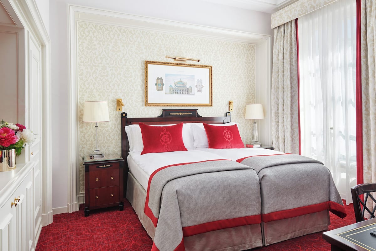 A hotel room with a large bed, two bedside tables, a nightstand, a framed picture on the wall, and a window with curtains.