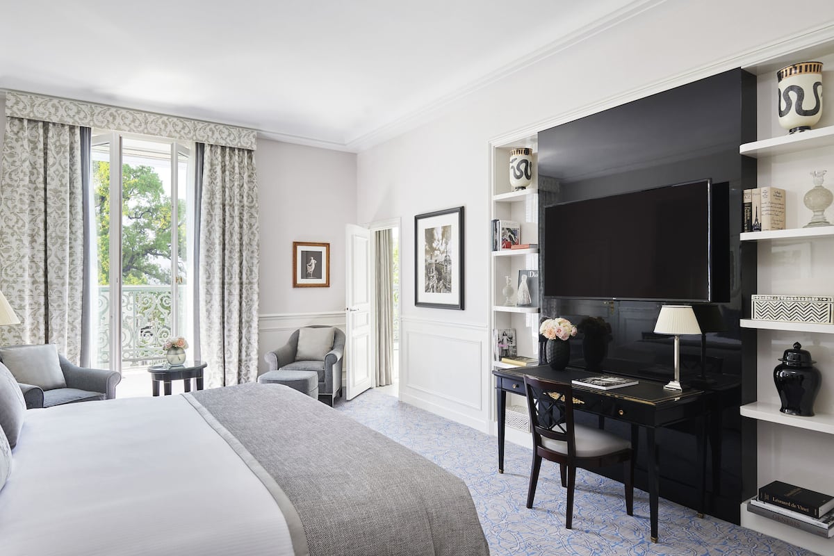 A hotel room with a bed, a desk, a chair, a TV, and a bookshelf.