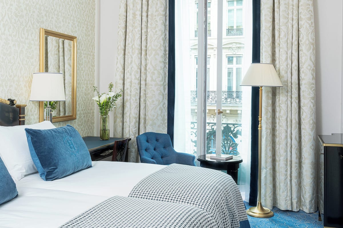 A hotel room with a bed, a chair, a desk, and a window with curtains.