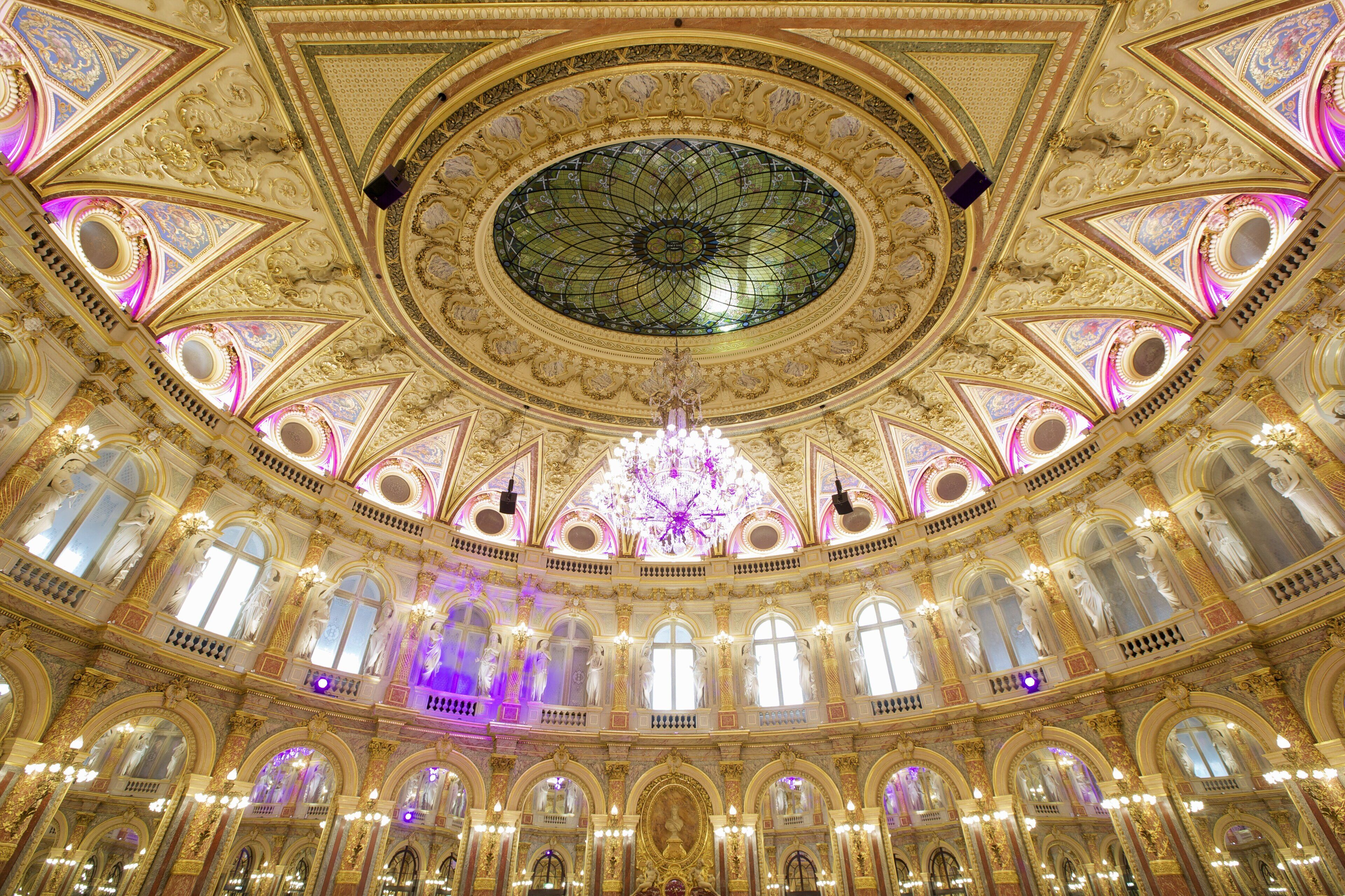 Un salón imponente con techo decorado, ventanas amplias y un candelabro central.
