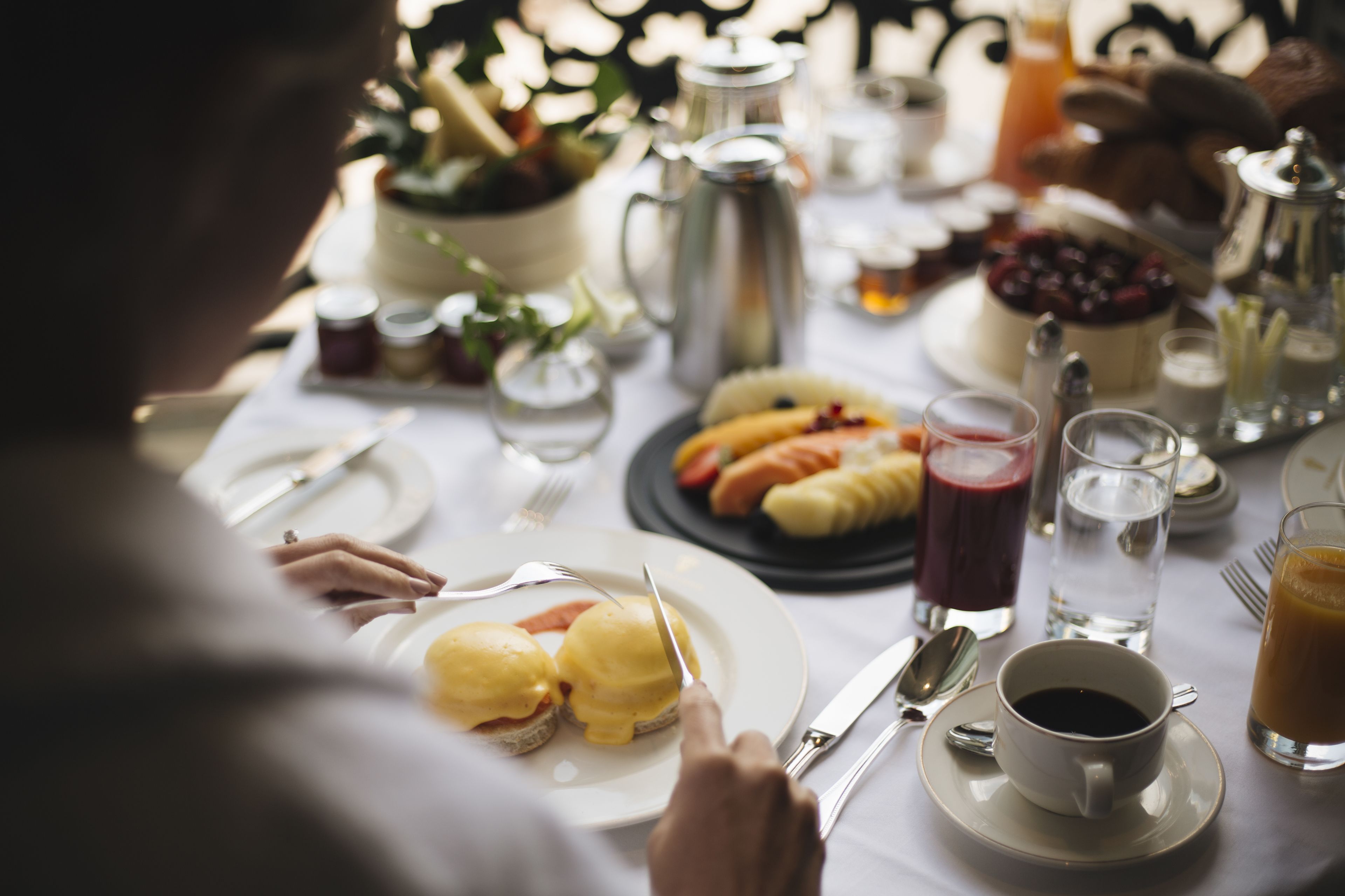 Una escena de desayuno con una mesa dispuesta para dos personas, que incluye platos con huevos Benedict, una taza de café y diversas opciones para el desayuno.