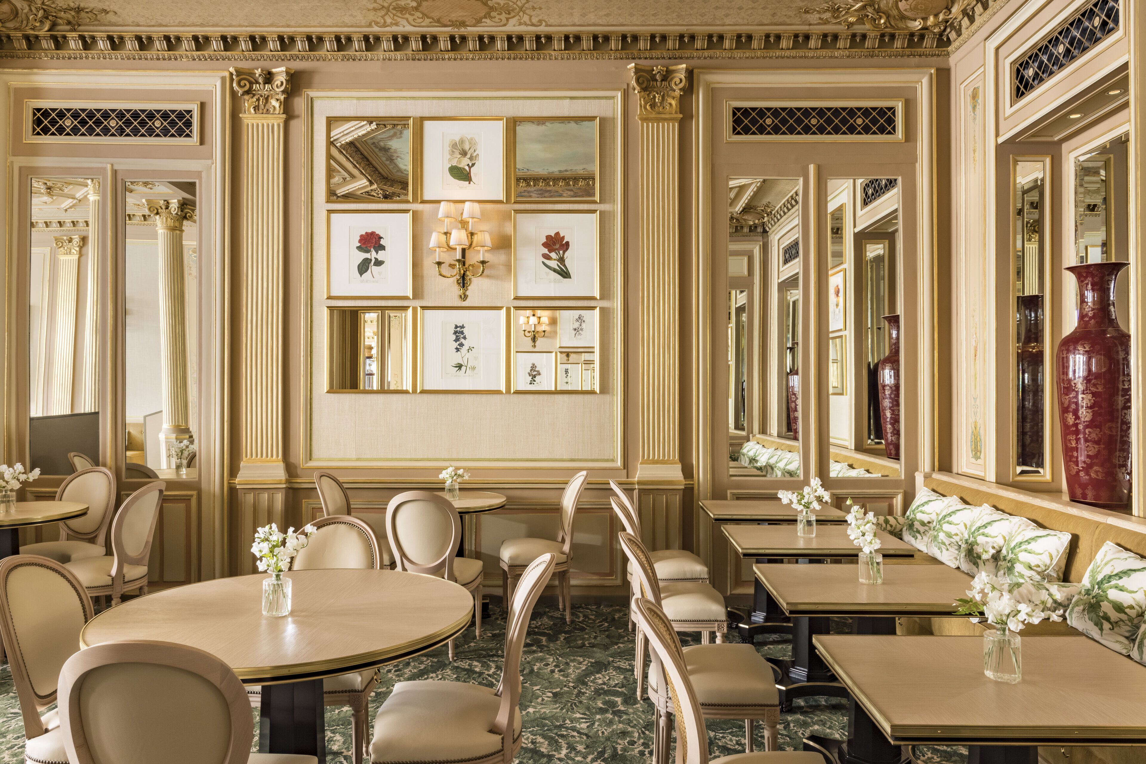 A formal dining room with multiple tables and chairs, framed artwork on the walls, and a large mirror reflecting the room.