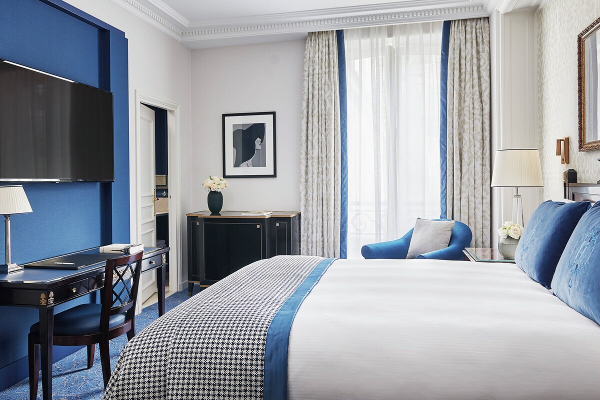 A hotel room with a large bed, a desk, a chair, a television, and a window with curtains.