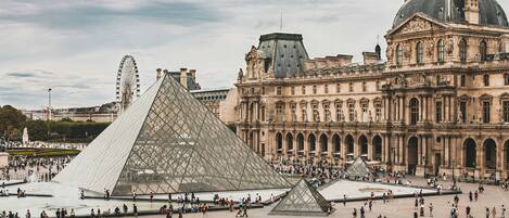 Una amplia plaza abierta con la Pirámide del Louvre y el Museo del Louvre al fondo.