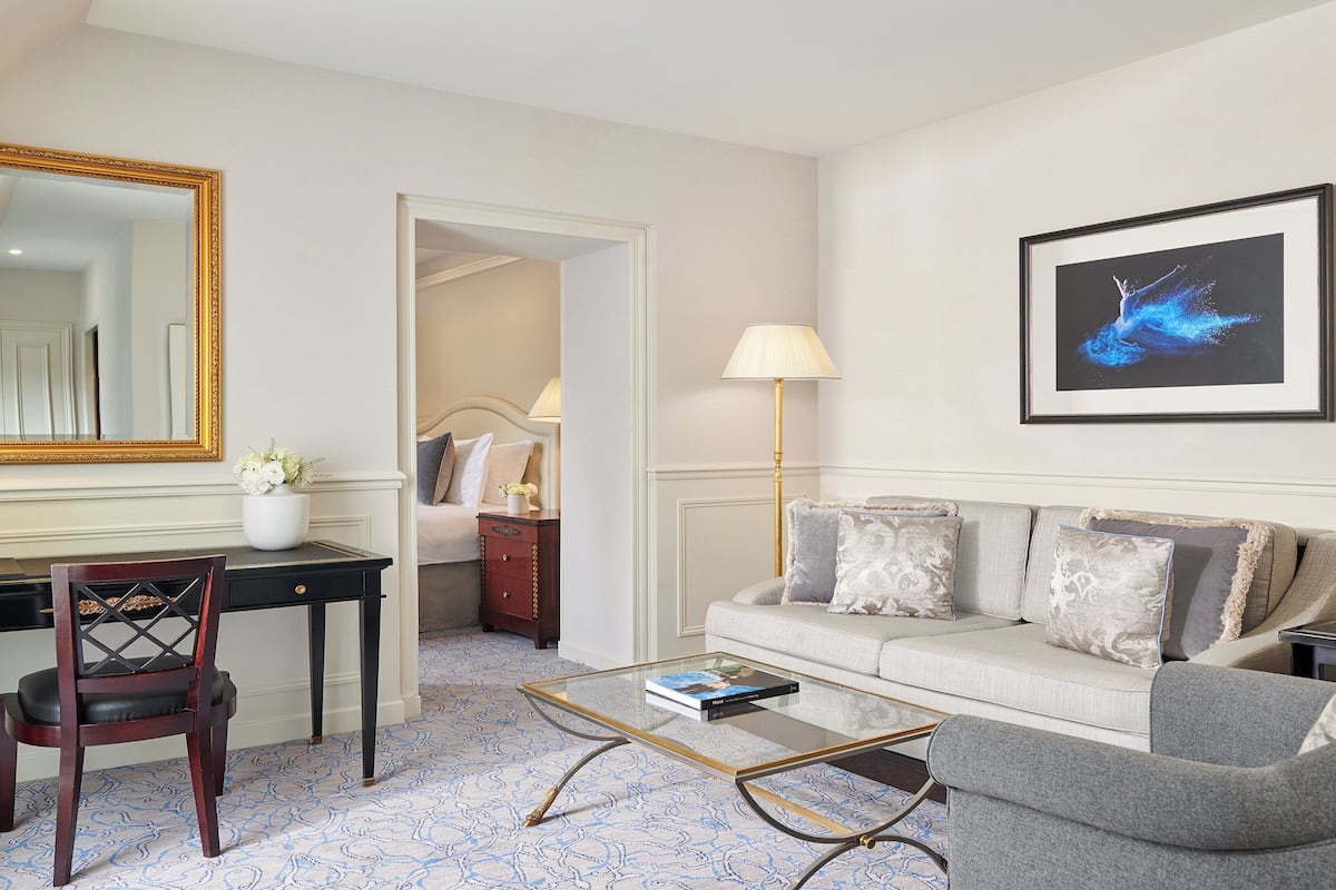 A hotel room with a desk, a glass coffee table, a sofa, a bed, and a large mirror.
