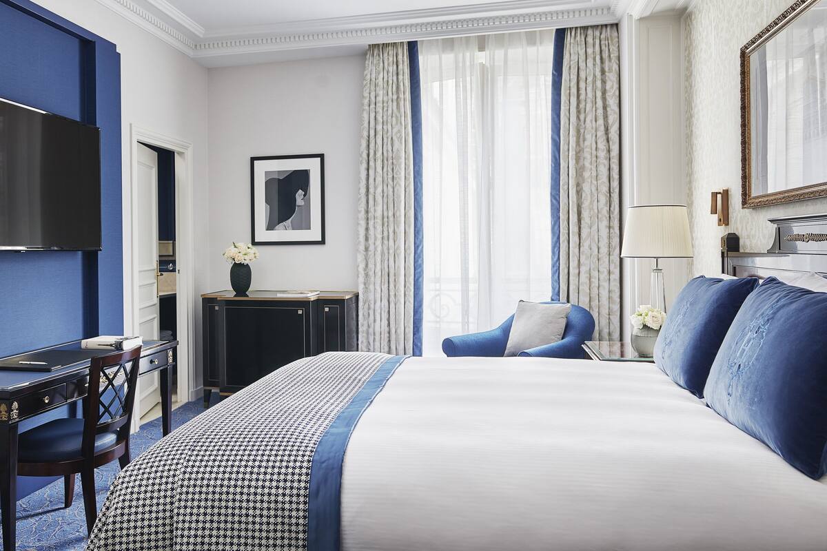 A hotel room with a large bed, a desk, a chair, a television, and a framed picture on the wall.