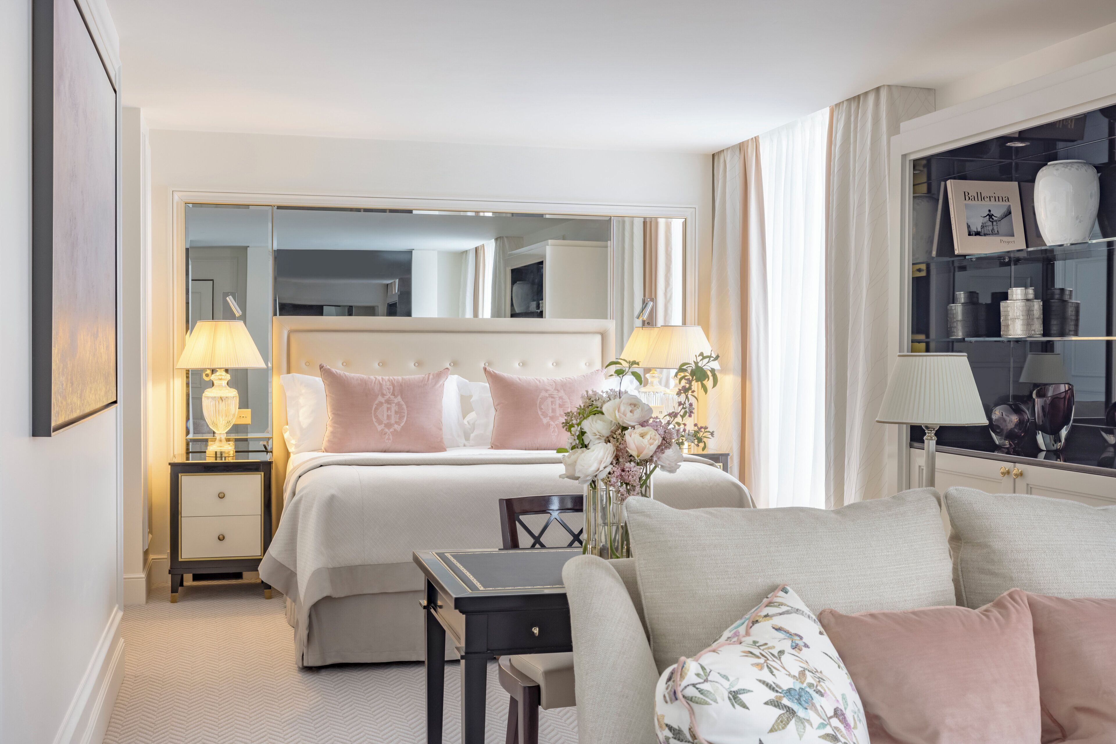 A hotel room with a bed, a nightstand, a desk, a chair, a mirror, and a shelf with decorative items.
