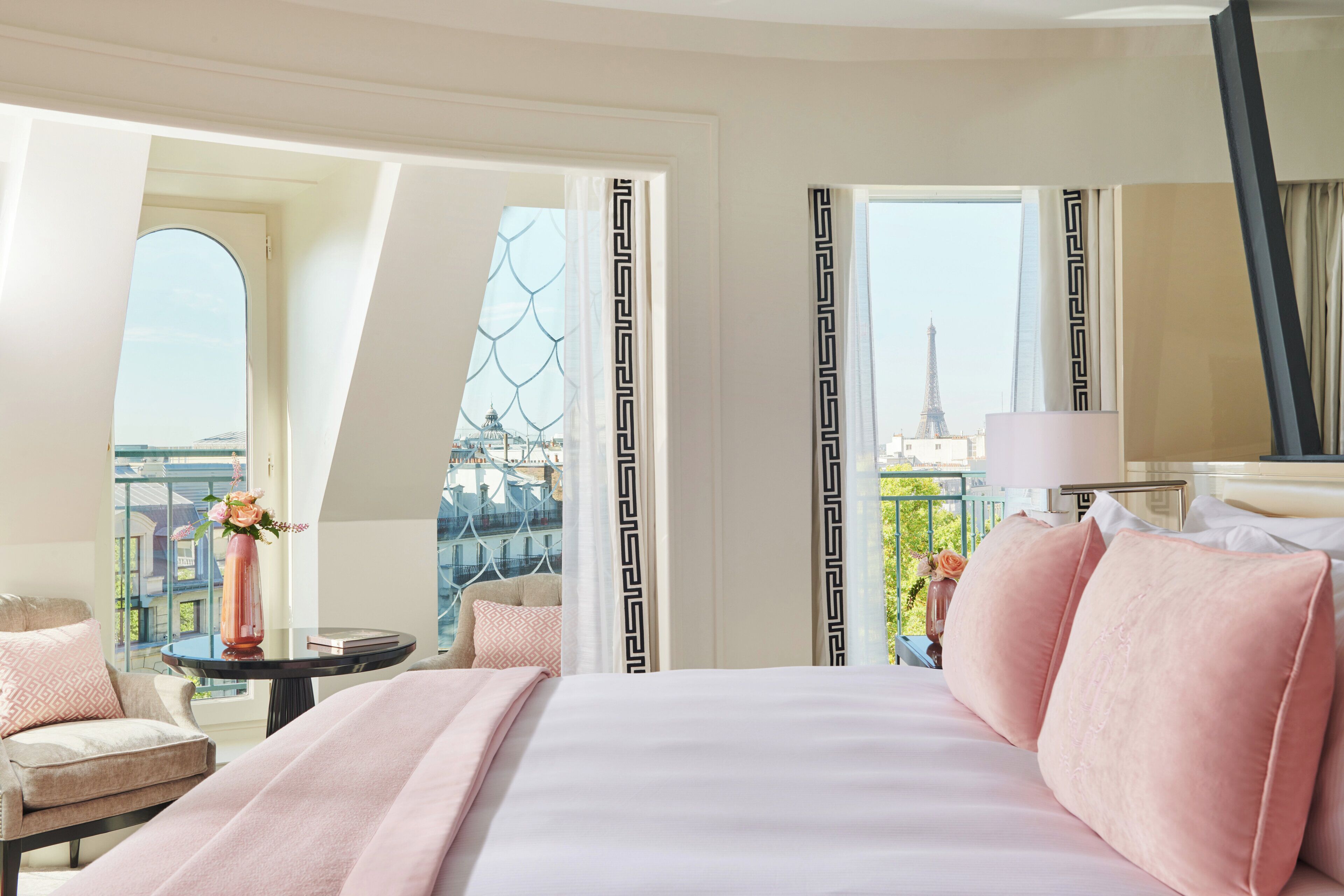 Ein Hotelzimmer mit einem Bett, einem Sessel, einem Tisch mit einer Vase und Blick auf den Eiffelturm.