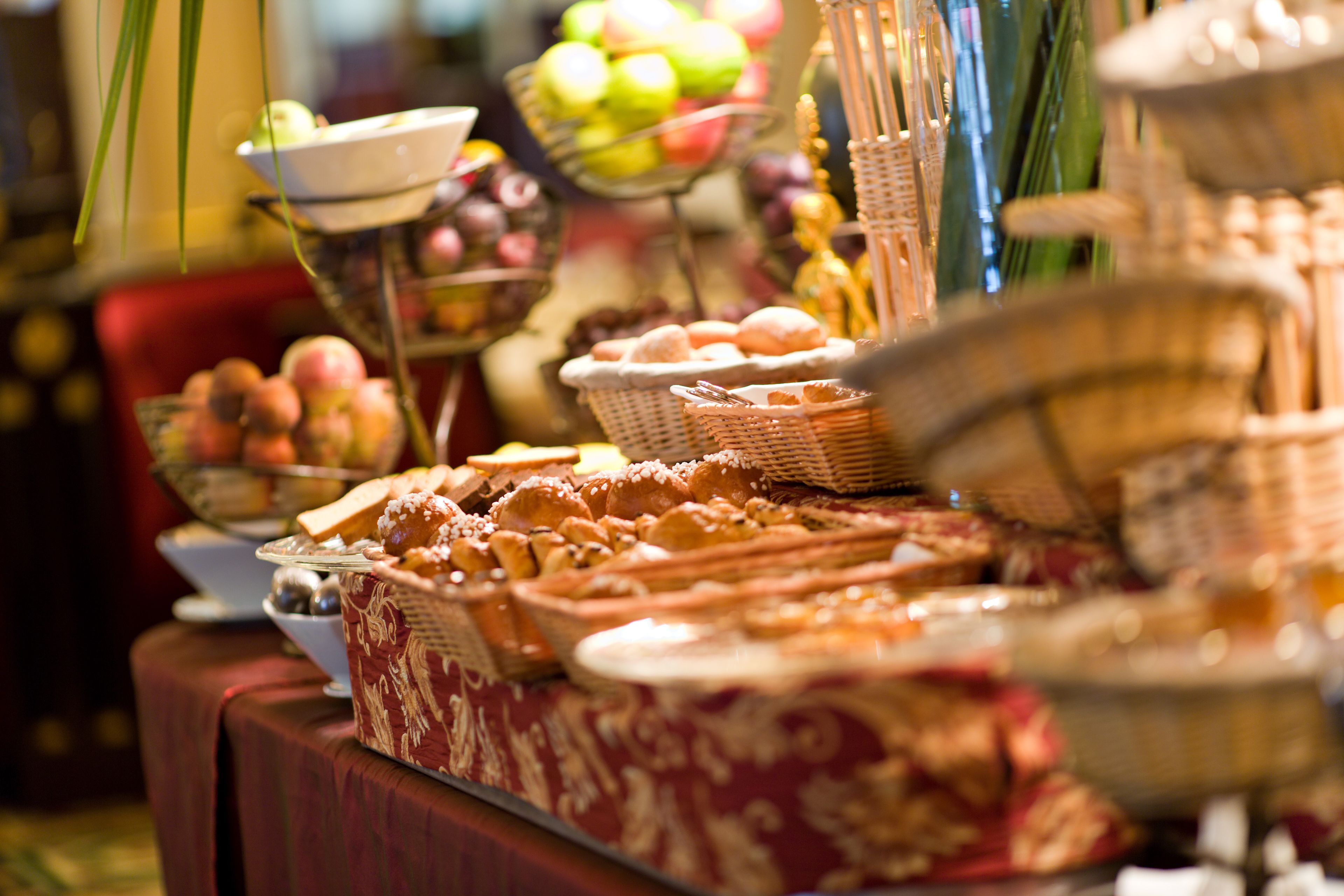 A buffet table with various food items and a bowl of fruit in the background.