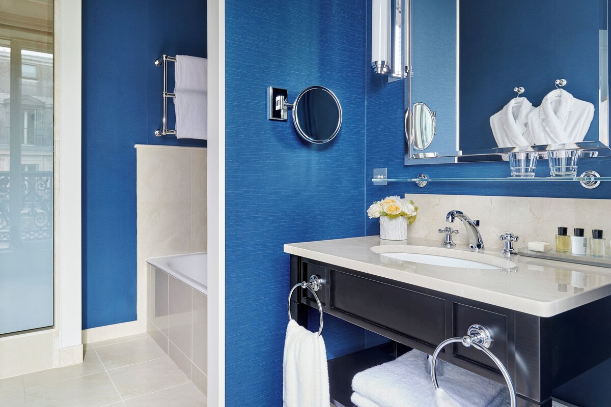 A modern bathroom with a blue accent wall, a bathtub, a sink with a mirror, and a towel rack.