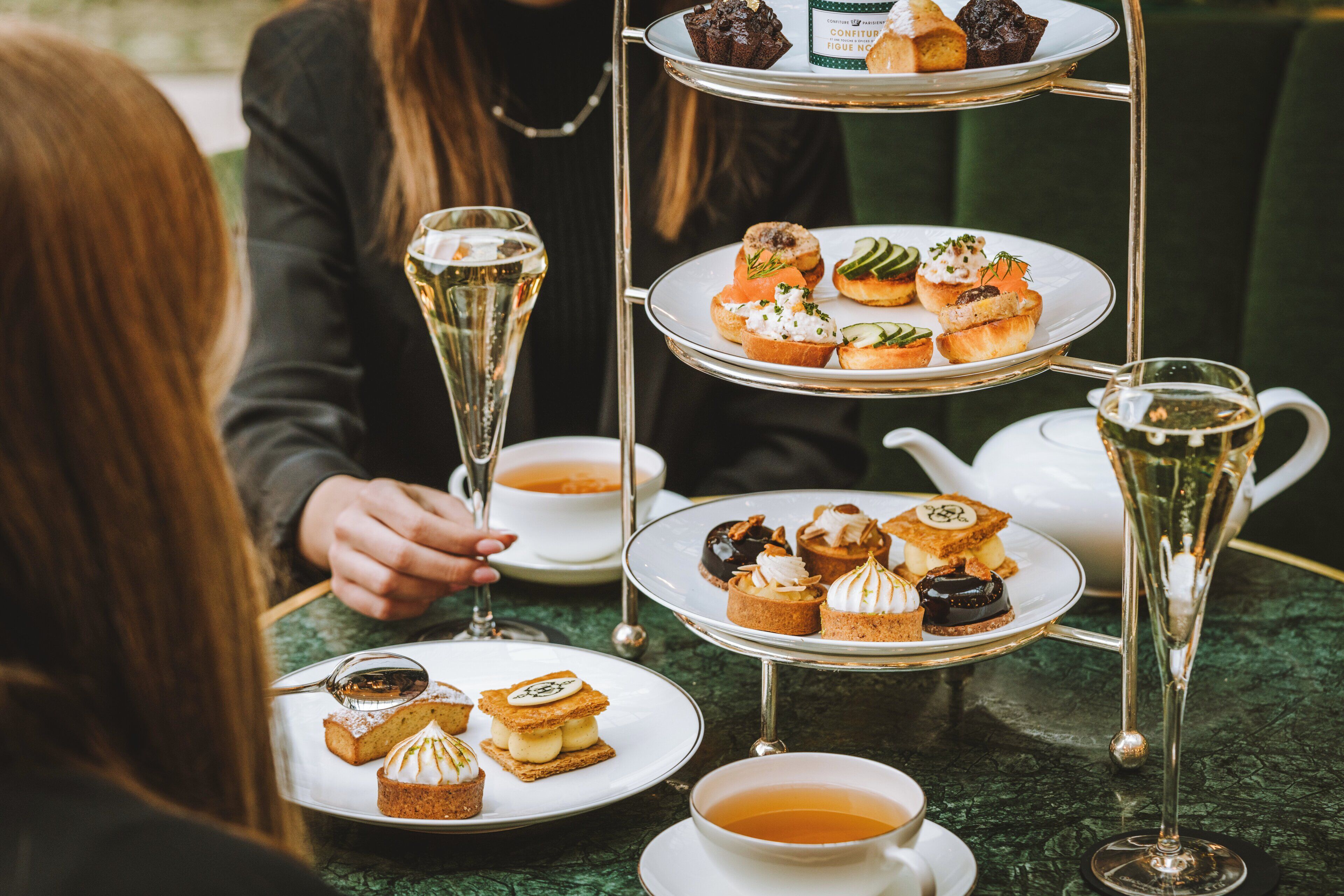 Un soporte escalonado para postres con diversos pasteles y una tetera sobre una mesa.