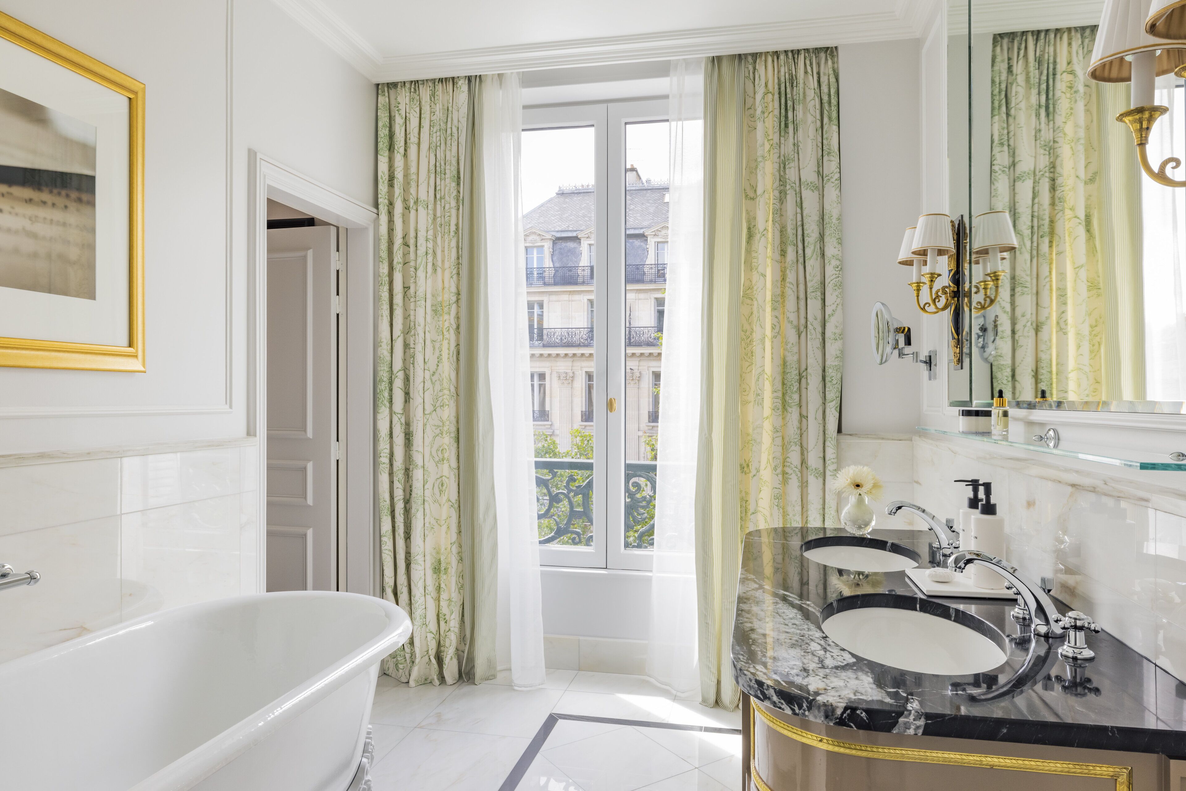 A bathroom with a bathtub, two sinks, a large mirror, and a view of a building through a window.