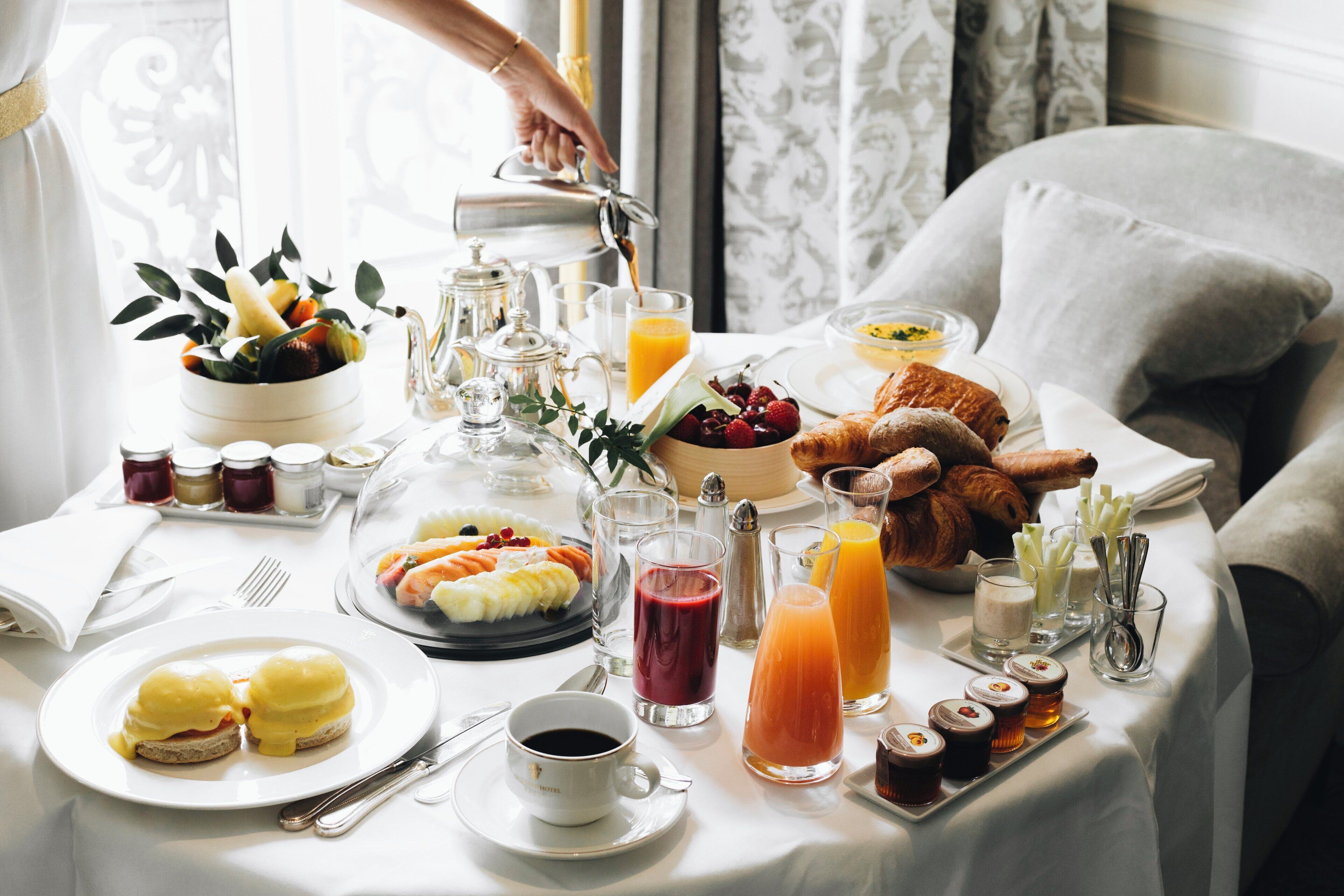 A breakfast table with various food items and beverages, including eggs, fruits, pastries, and coffee.