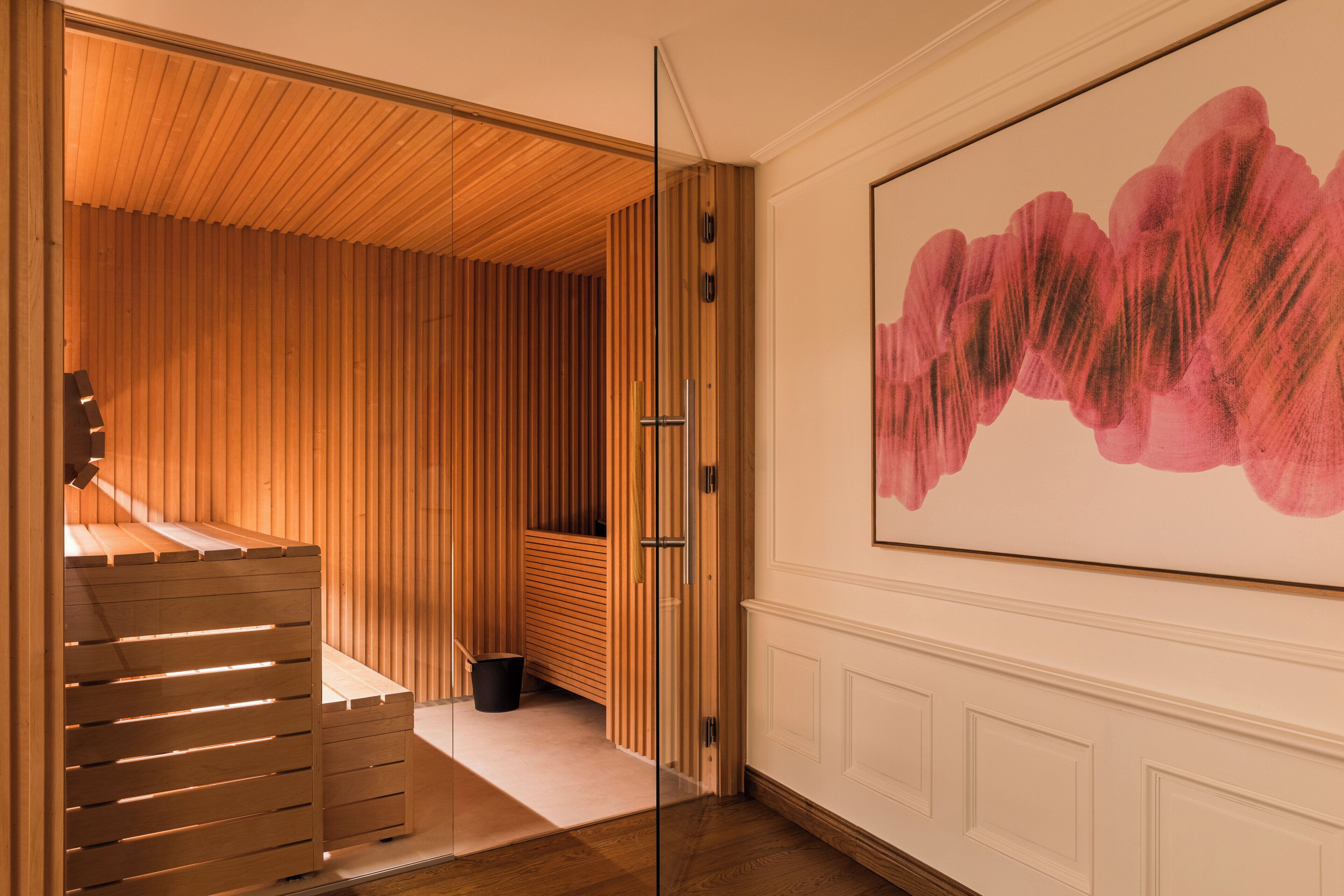 A modern interior with a wooden slatted wall, a glass partition, and a large abstract painting.