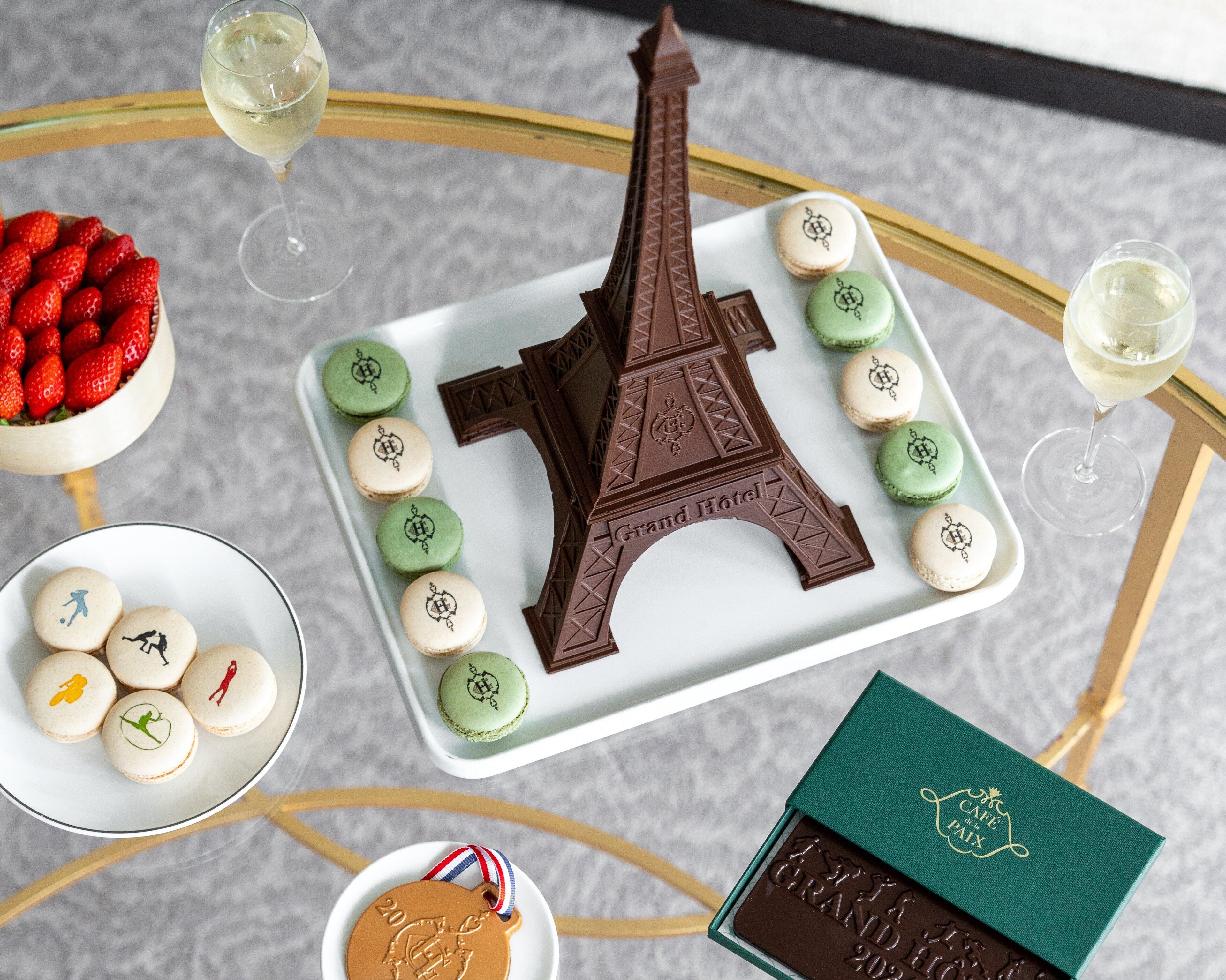 A table with macarons, a chocolate Eiffel Tower, a medal, and a box of chocolate.