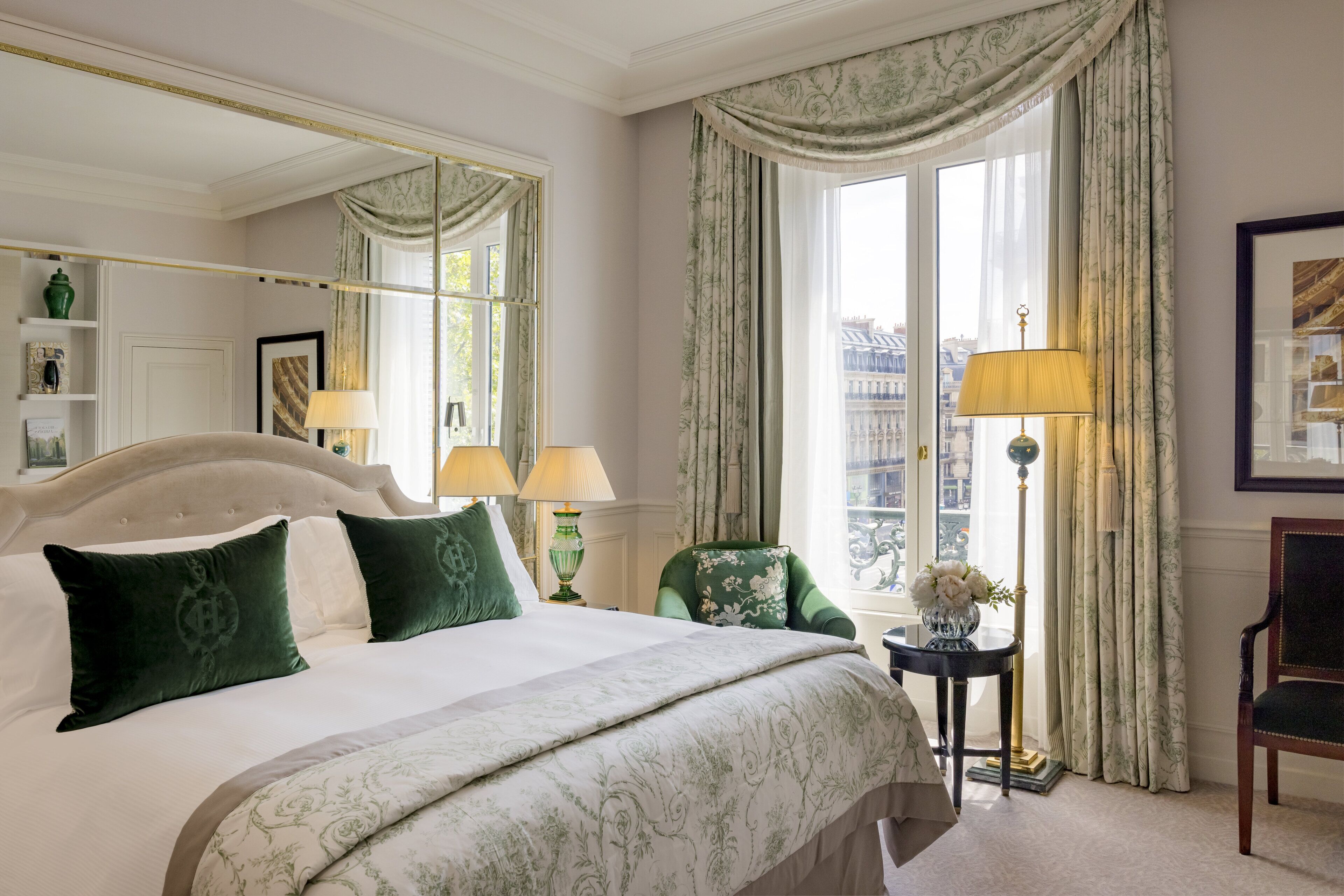 A hotel room with a large bed, two lamps, a chair, and a view of the city.