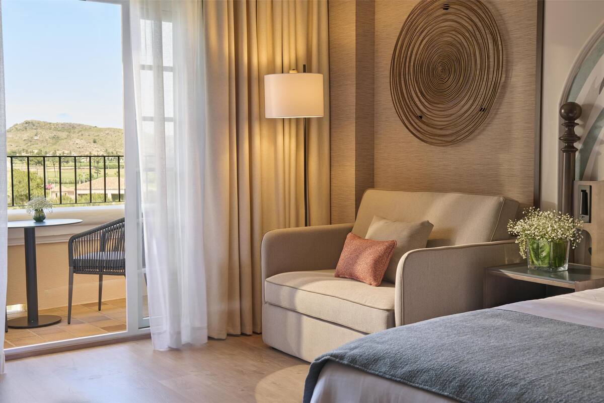 Une chambre d’hôtel avec un lit, un canapé, une table ornée d’un vase de fleurs, une lampe et une vue sur l’extérieur.