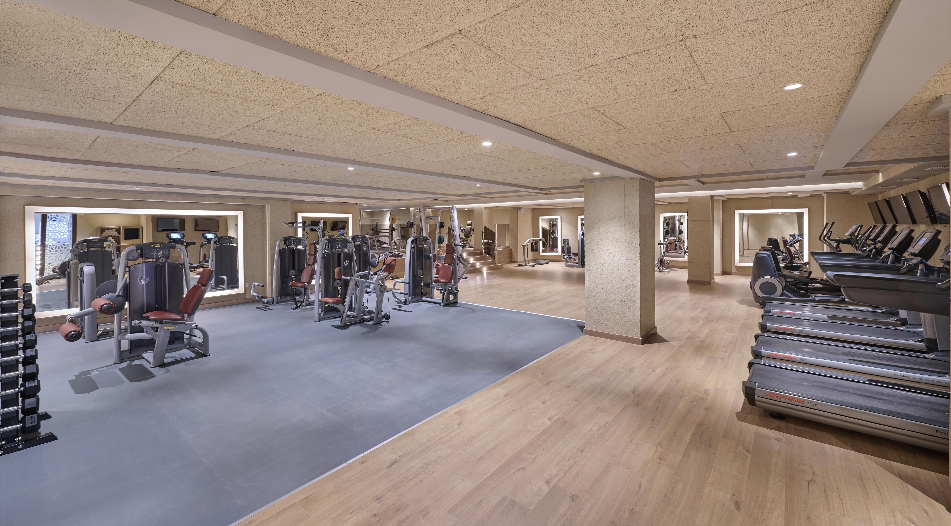 Un gimnasio espacioso con máquinas de cardio, estaciones de pesas y un espejo grande.