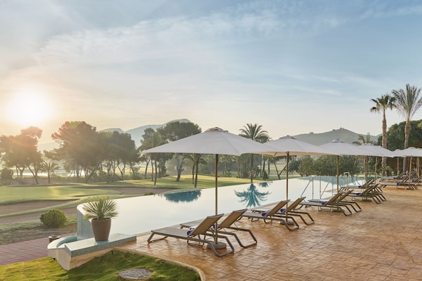 Una piscina al aire libre, sombrillas, sillones reclinables de piscina