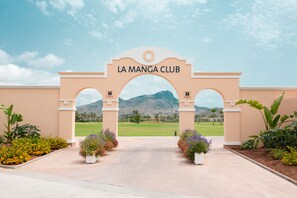 Enter La Manga Club through a distinctive archway, surrounded by lush gardens and vibrant flower beds.