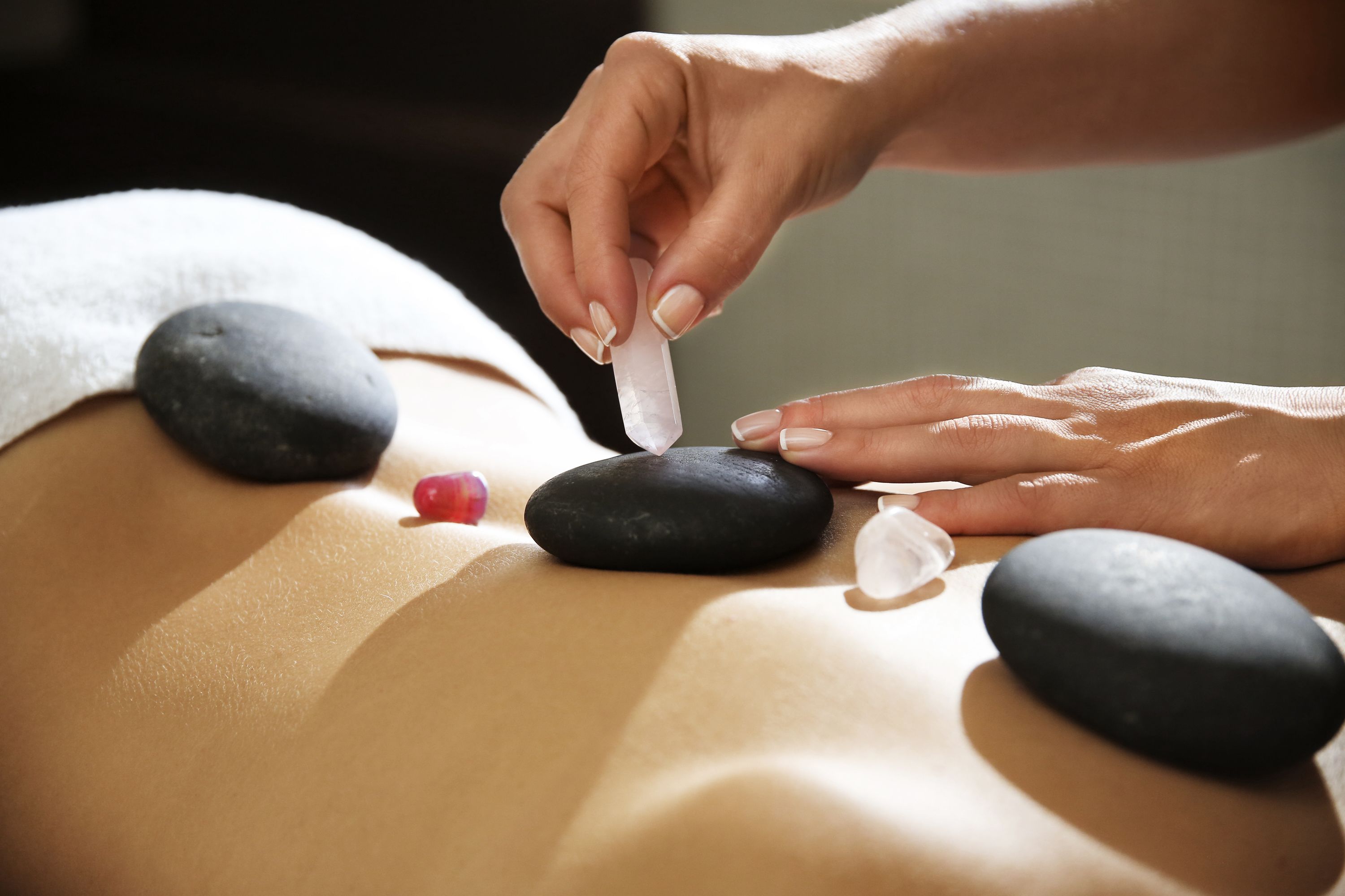 A person receiving a stone massage with black stones and a clear crystal on their back.