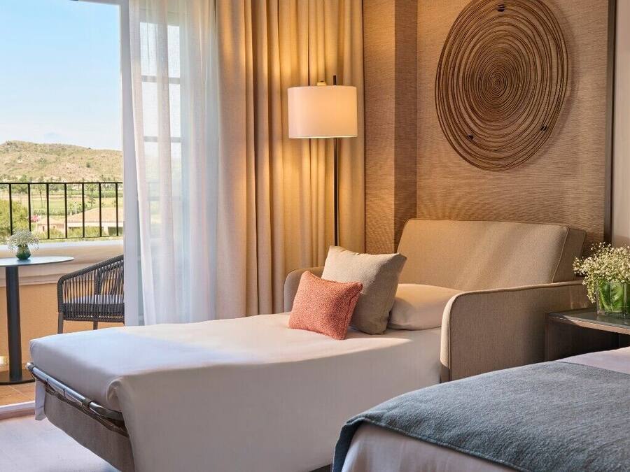 Habitación de hotel con dos camas, un balcón con mesa y silla, una lámpara y un adorno en la pared.