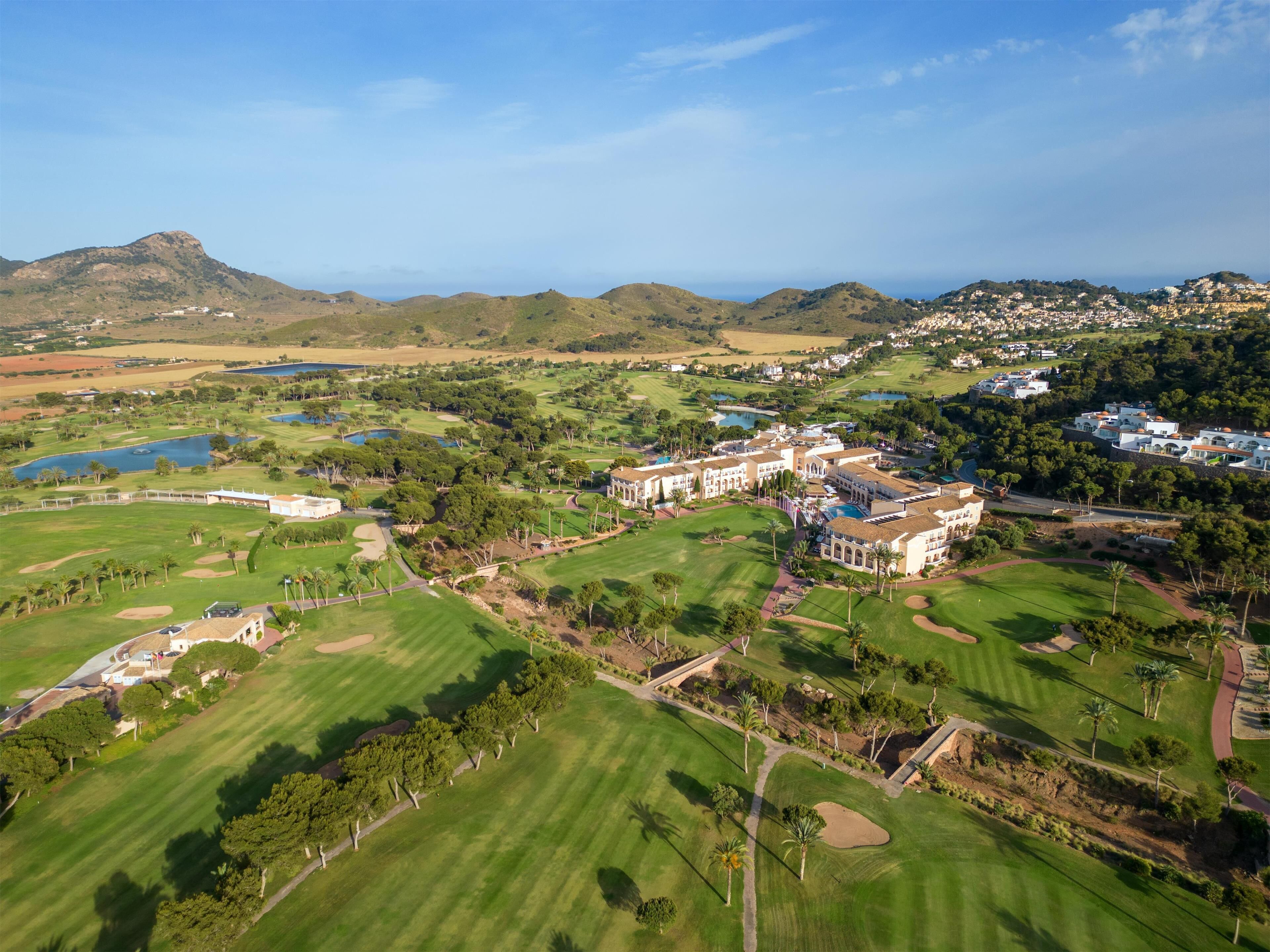 An aerial view of a golf course with a clubhouse, multiple water bodies, and surrounding hills.
