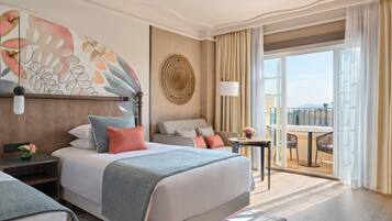 A hotel room with a large bed, a sofa, a small table, and a balcony with a view.