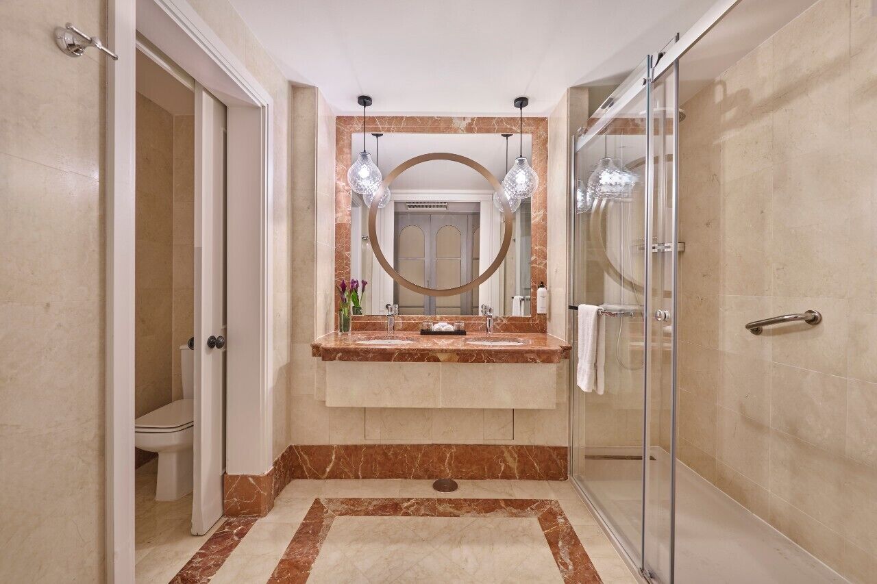 A modern bathroom with a glass shower enclosure, a marble vanity, and a large mirror with pendant lighting.