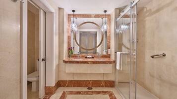 A modern bathroom with a glass shower enclosure, a marble vanity, and a large mirror with pendant lighting.