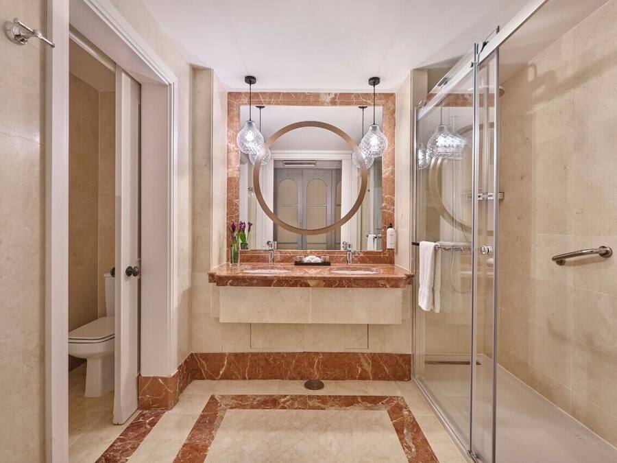 A modern bathroom with a glass shower enclosure, a marble vanity, and a large mirror with pendant lighting.