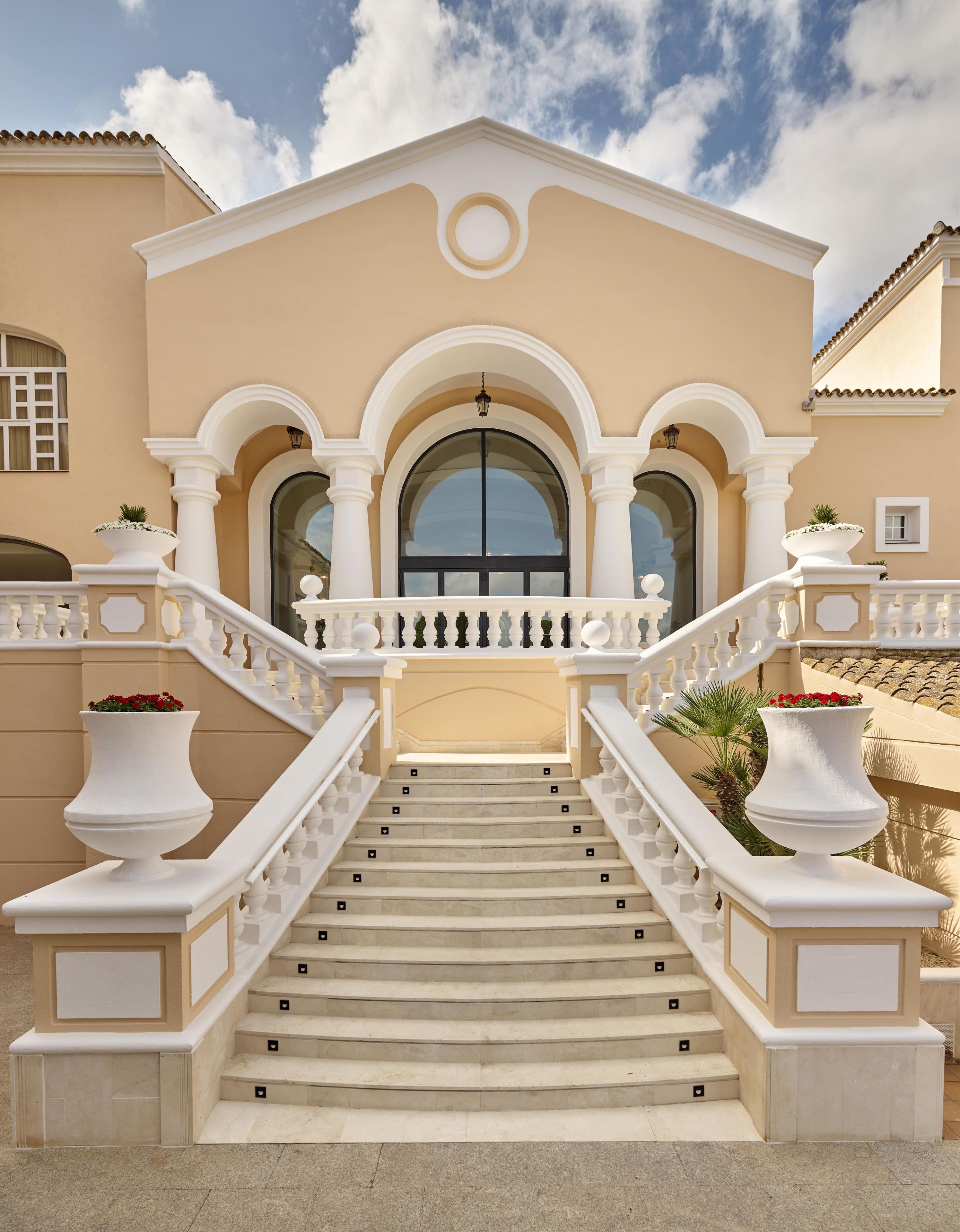 Una entrada imponente con una escalera que conduce a una puerta, flanqueada por balaustradas blancas y grandes macetas.
