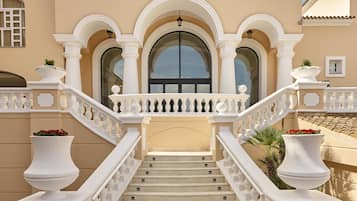 Una entrada imponente con una escalera que conduce a una puerta, flanqueada por balaustradas blancas y grandes macetas.