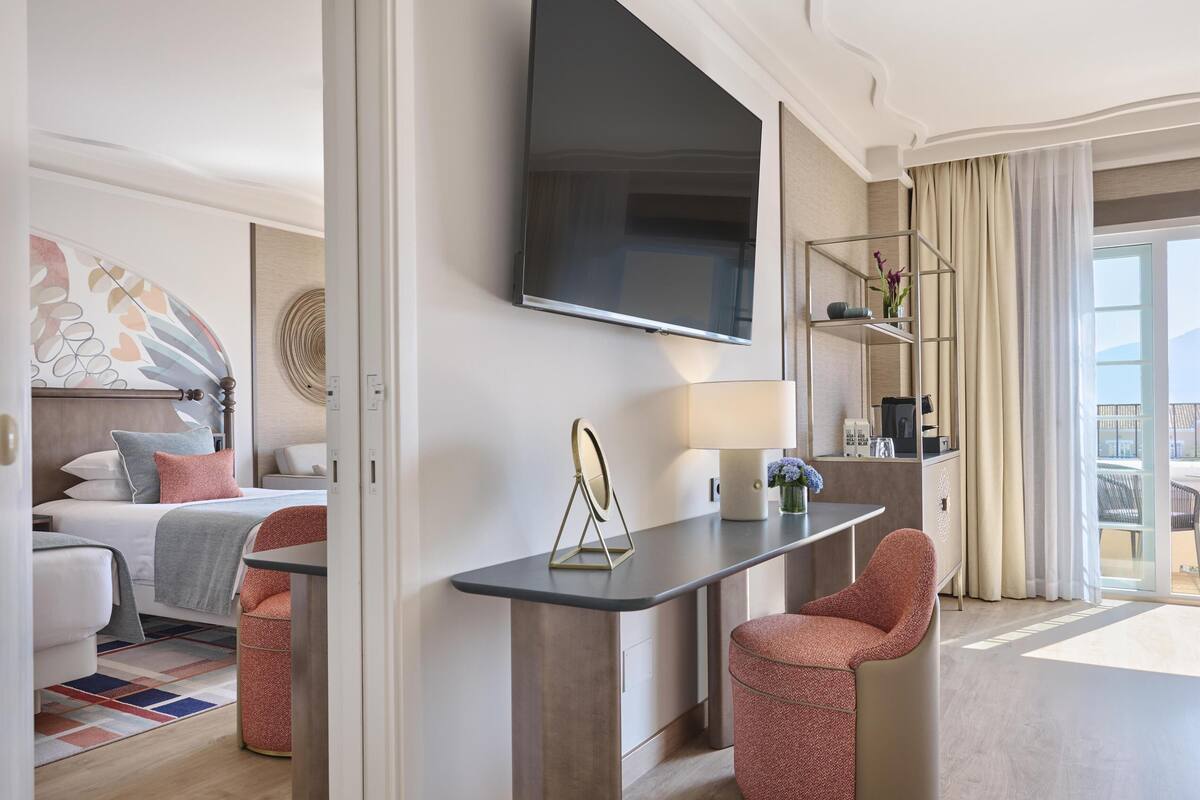 Une chambre d’hôtel moderne équipée d’un lit, d’un bureau, d’une chaise, d’une télévision et d’un balcon avec des rideaux.