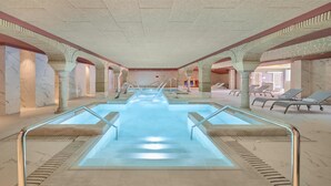 Ein Innenpool mit Marmorwänden und -säulen, umgeben von Liegestühlen.
