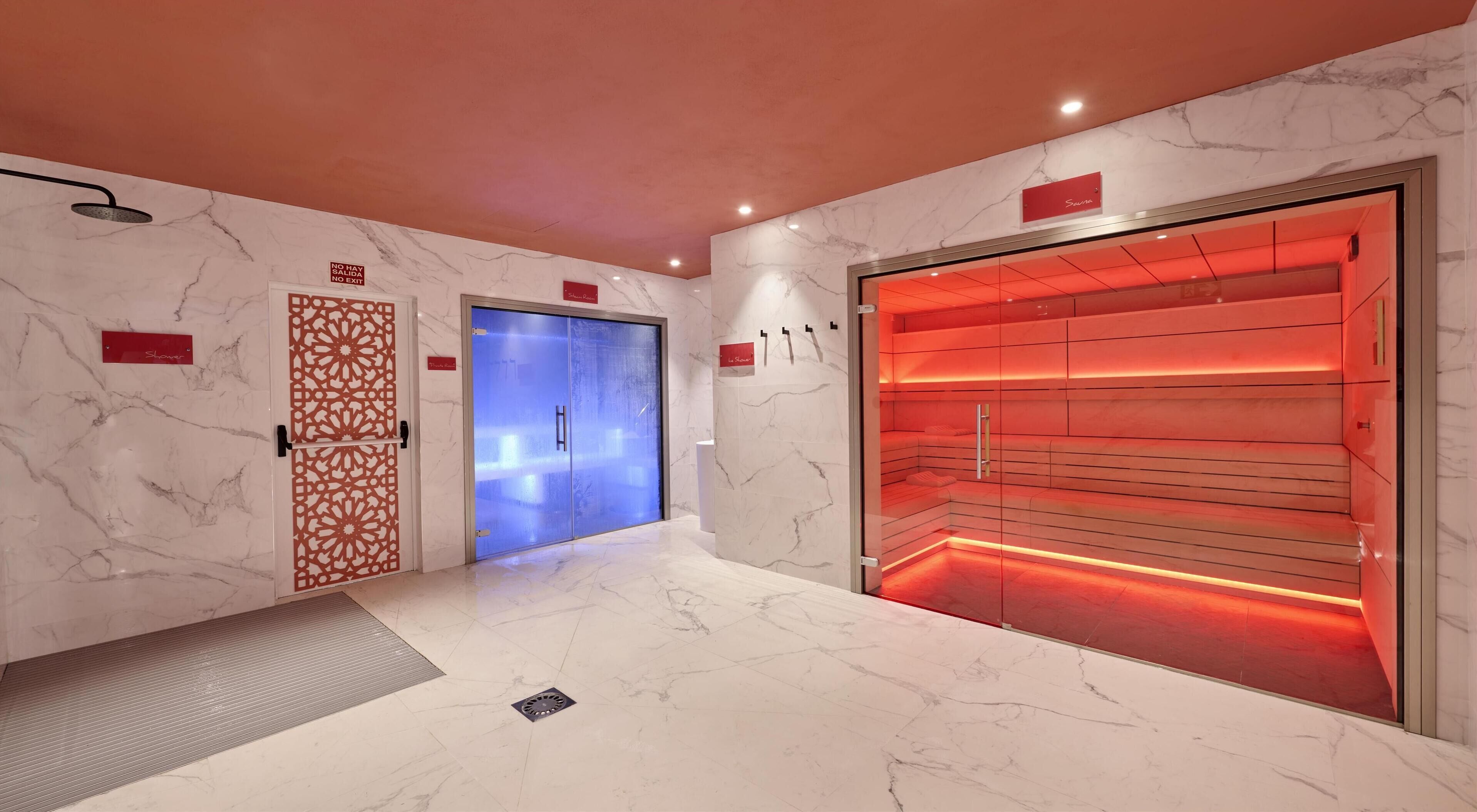 Un área de spa con una puerta azul, una sauna iluminada con luz roja y una pared de mármol.