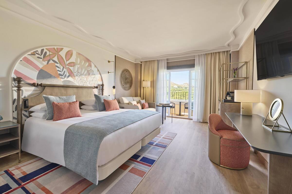 Une chambre d’hôtel moderne avec un grand lit, un bureau, une chaise et un balcon offrant une vue agréable.
