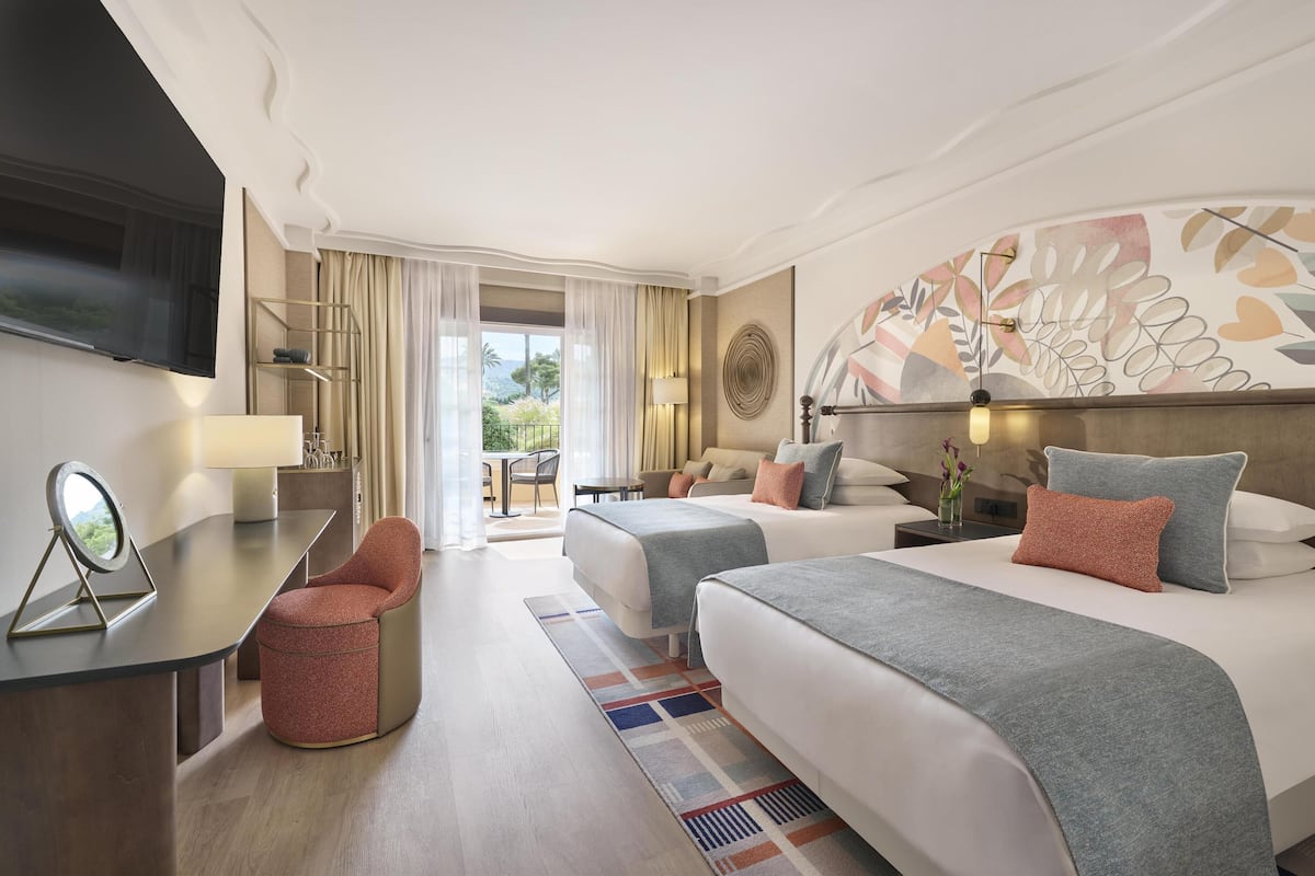 Une chambre d’hôtel avec deux lits, un bureau avec un miroir, une télévision et une vue sur l’extérieur.