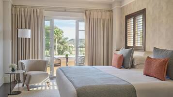 Habitación de hotel con una cama grande, una silla, una mesita y un balcón con vistas a zonas verdes.