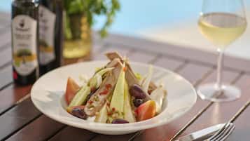 A plate of salad with a glass of white wine and bottles of wine on a wooden table.