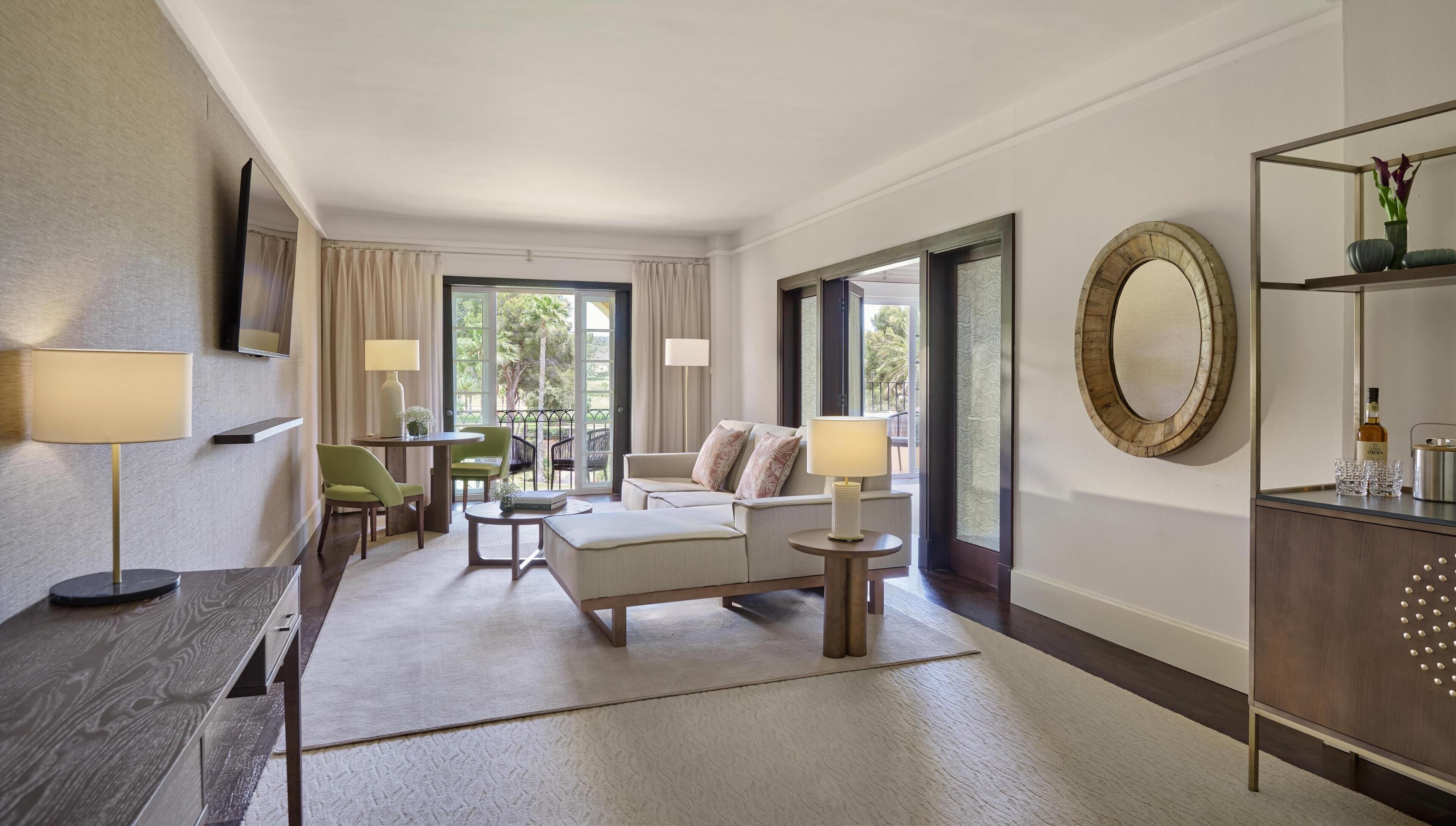 Une chambre d’hôtel avec un canapé, des fauteuils, une table, une lampe, un miroir et une vue sur l’extérieur.