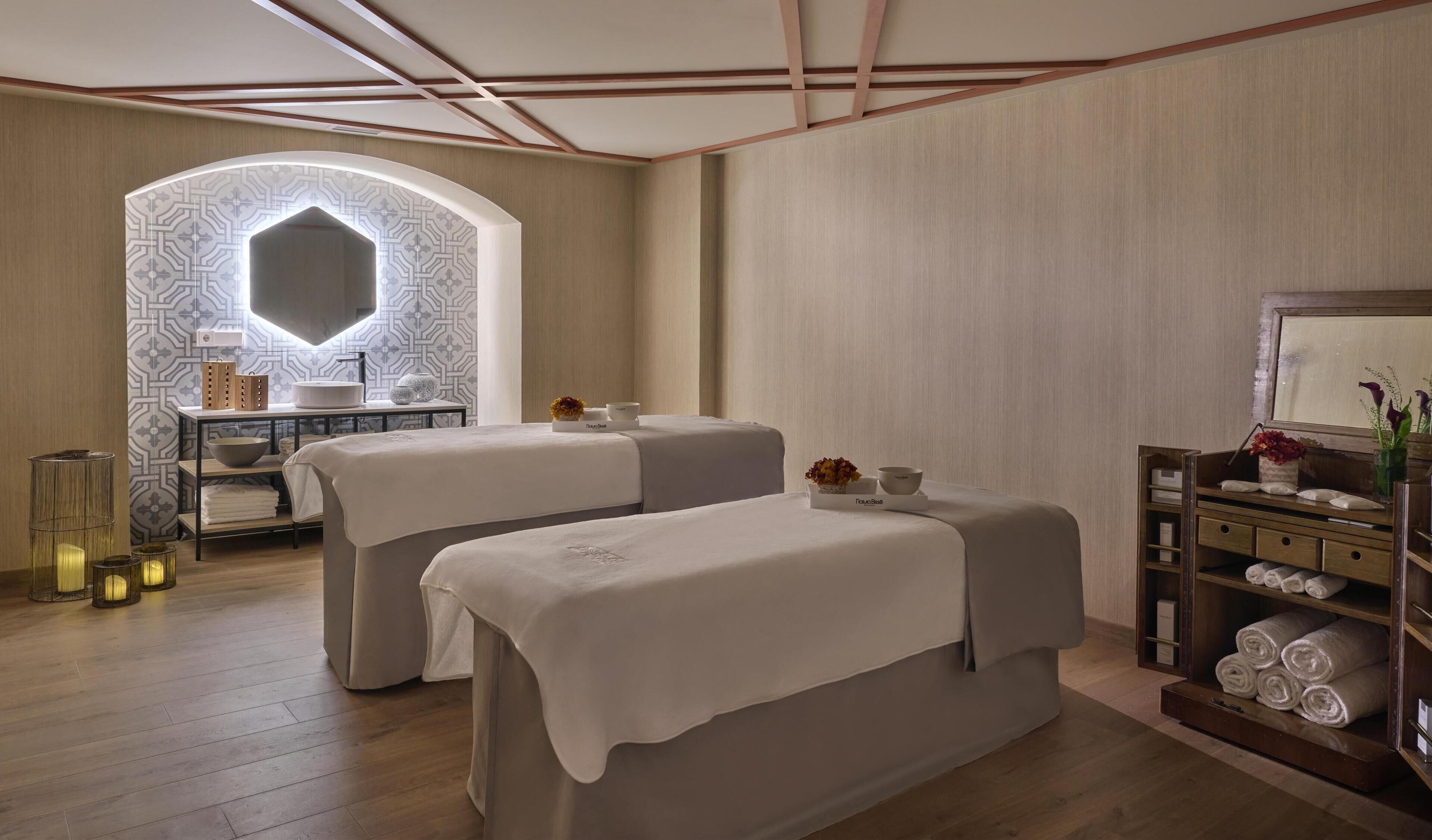 Un cuarto de spa con dos camillas de masaje, un tocador con espejo y un estante con toallas.