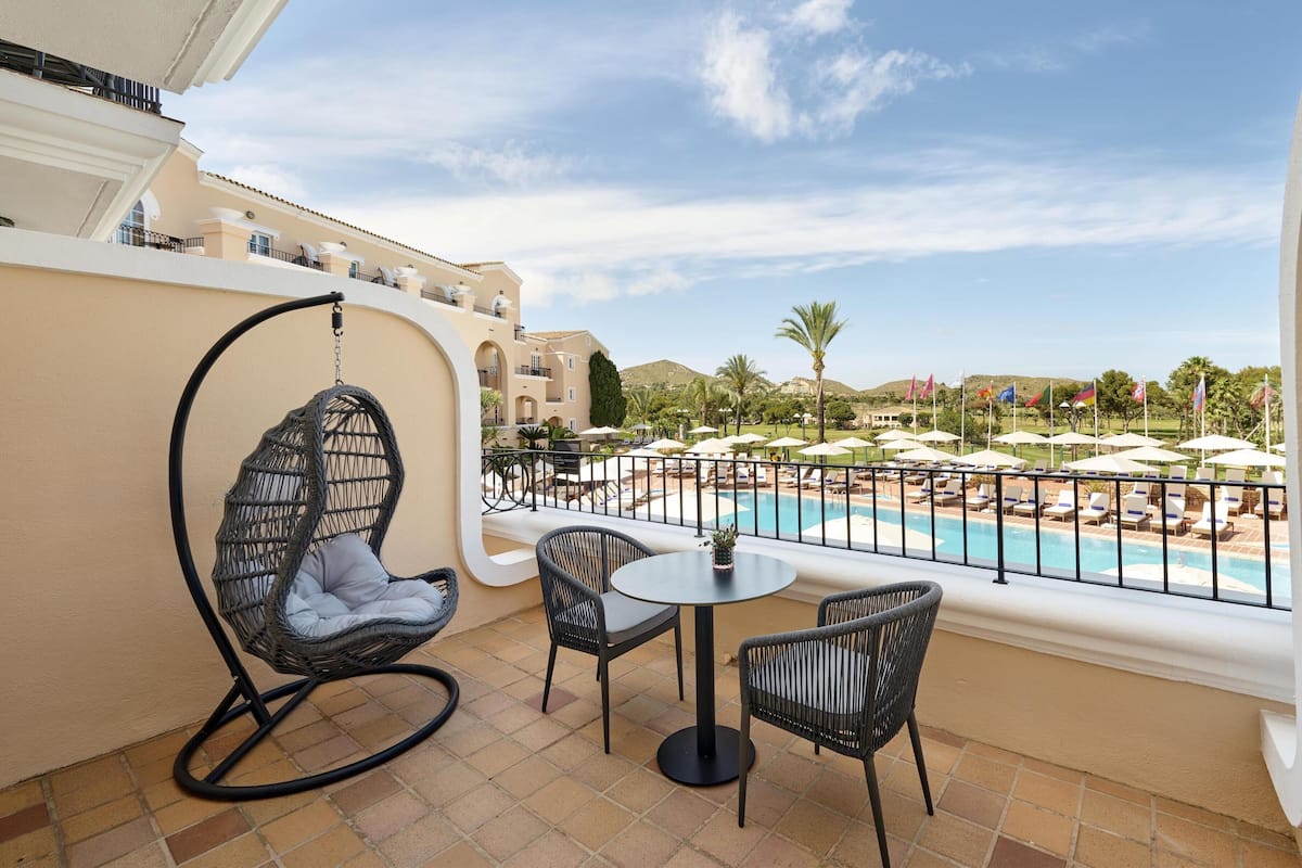 Un balcon agrémenté d’un fauteuil suspendu, de deux chaises, d’une petite table et offrant une vue sur une piscine et un espace de détente.