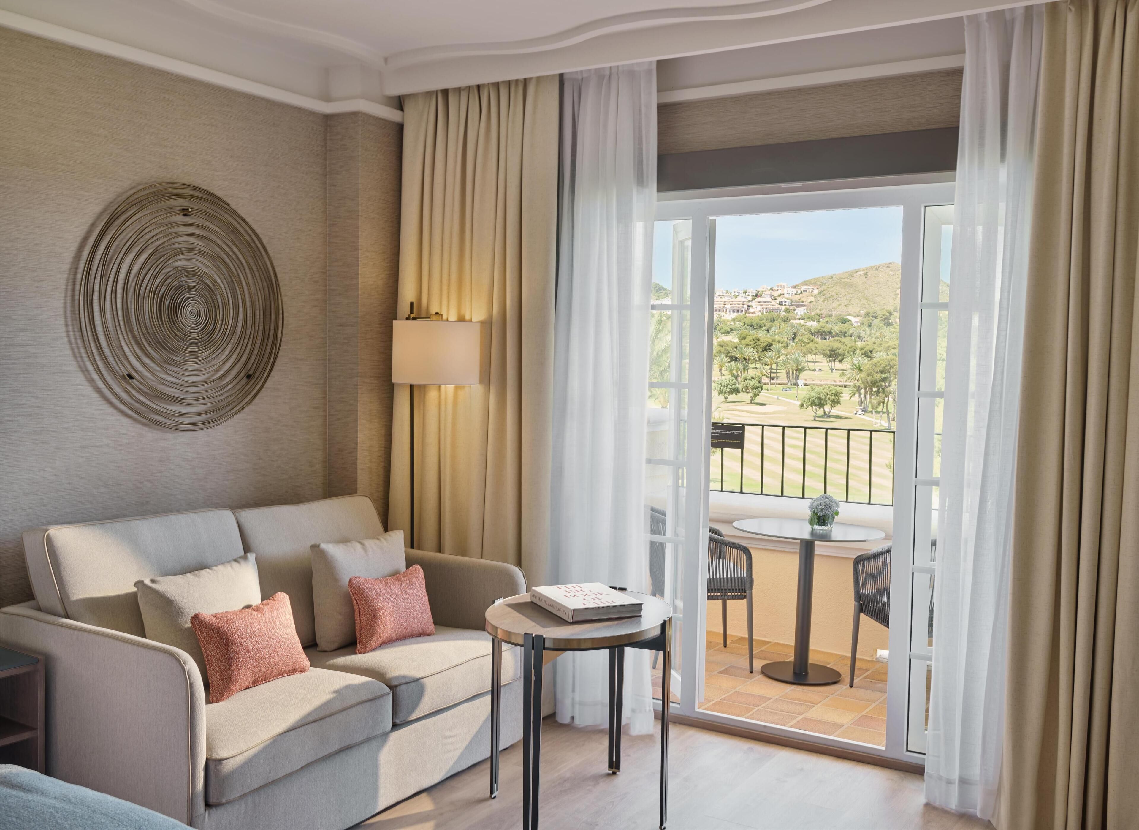 Une chambre d’hôtel moderne, dotée d’un canapé, d’une petite table et offrant une vue sur un terrain de golf grâce à une porte-fenêtre coulissante.