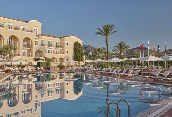 Un hotel con zona de piscina, tumbonas, sombrillas y banderas.