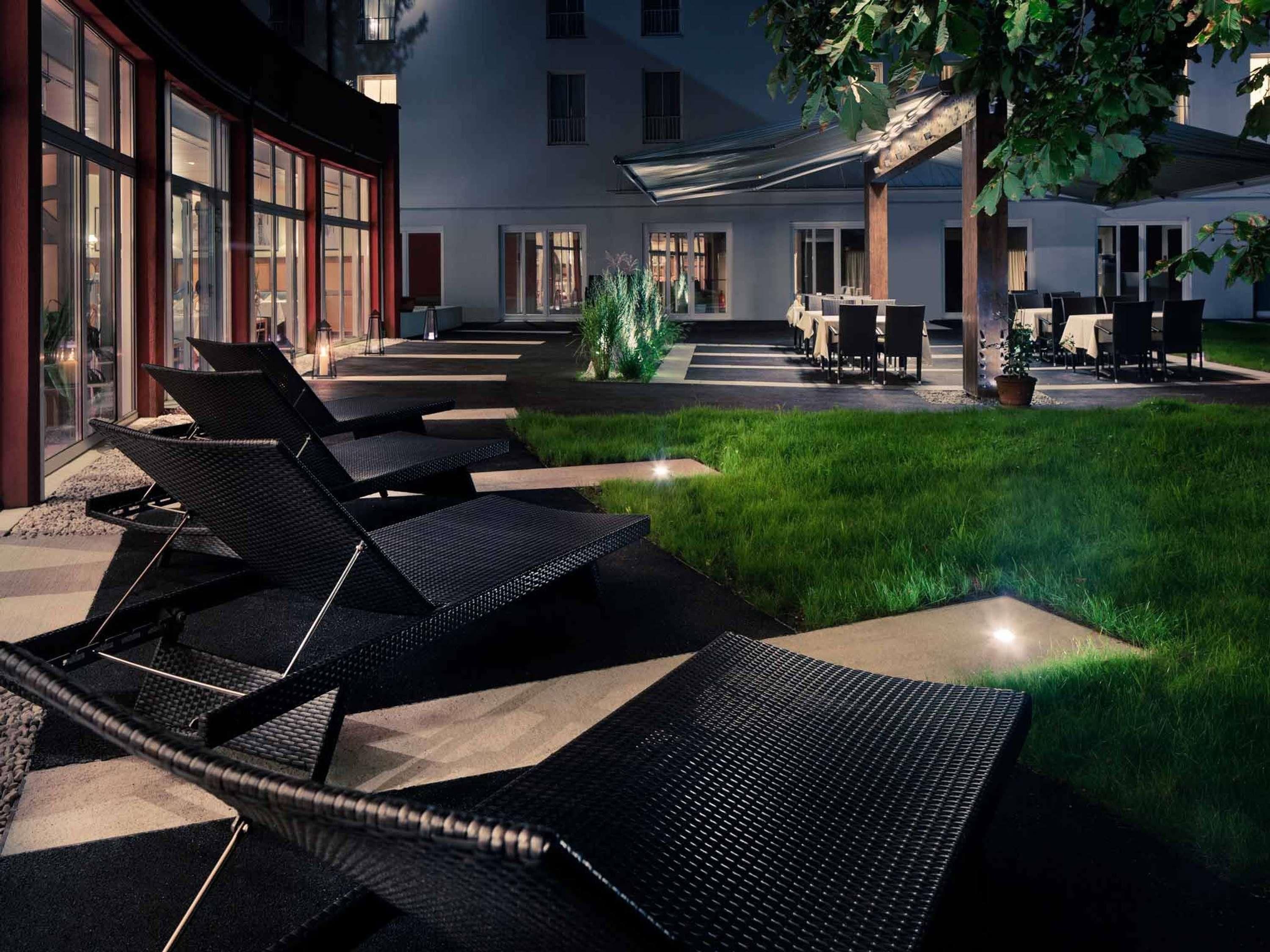Un patio con mesas al aire libre, un edificio con amplios ventanales y un árbol.