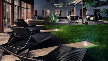 Un patio con mesas al aire libre, un edificio con amplios ventanales y un árbol.