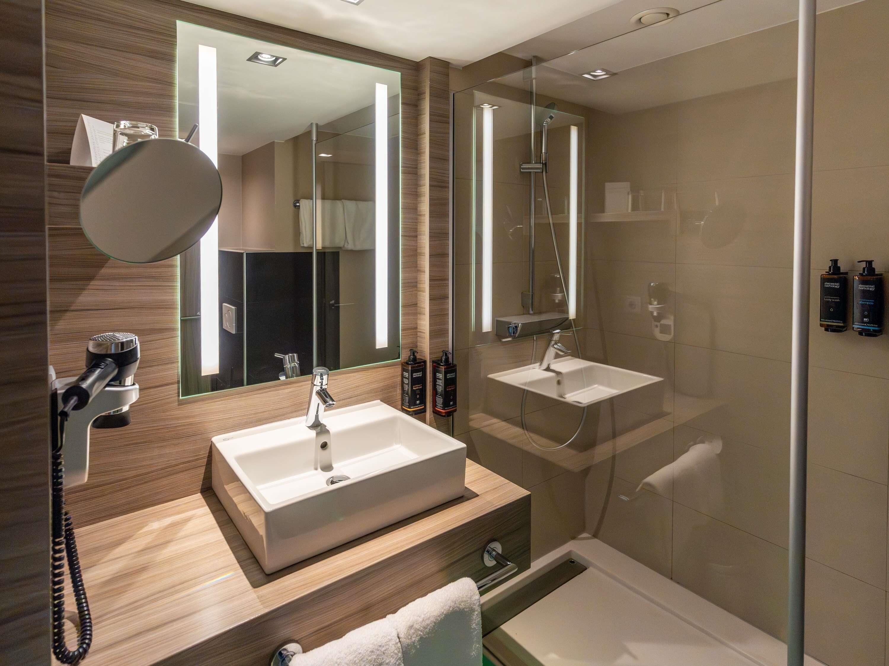 Un baño moderno con un espejo grande, dos lavamanos, una ducha y un teléfono.