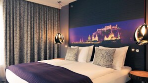 A hotel room with a large bed, a cityscape mural, and two pendant lights. - Mercure Salzburg City (Salzburg)